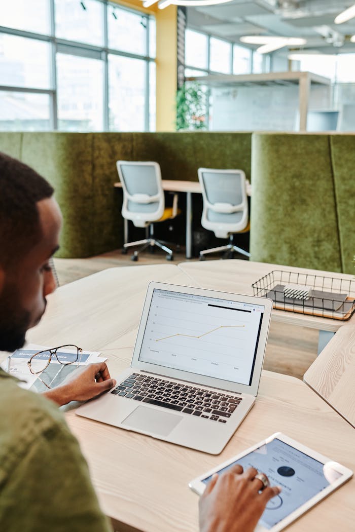 Man analyzing graphs on a laptop and tablet in a modern office setting.